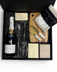 Luxury gift box featuring Pol Roger Champagne, quality champagne glasses, Loco Love artisan chocolate, hand-printed linen tea towel, Ecosoy candle, artisan soap and cheese knives styled on a neutral linen backdrop