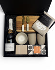 Luxury corporate gift box with Pol Roger Champagne, Koko Black chocolates, hand-printed linen tea towel, handcrafted ceramic dishes and cups, eco-soy candle, wood board and cheese knives, elegantly arranged