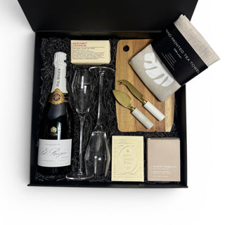 Luxury gift box featuring Pol Roger Champagne, quality champagne glasses, Loco Love artisan chocolate, hand-printed linen tea towel, Ecosoy candle, artisan soap and cheese knives styled on a neutral linen backdrop